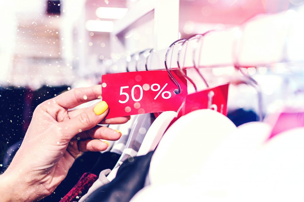 person holding red and white discount label on clothes hangar in a retail store